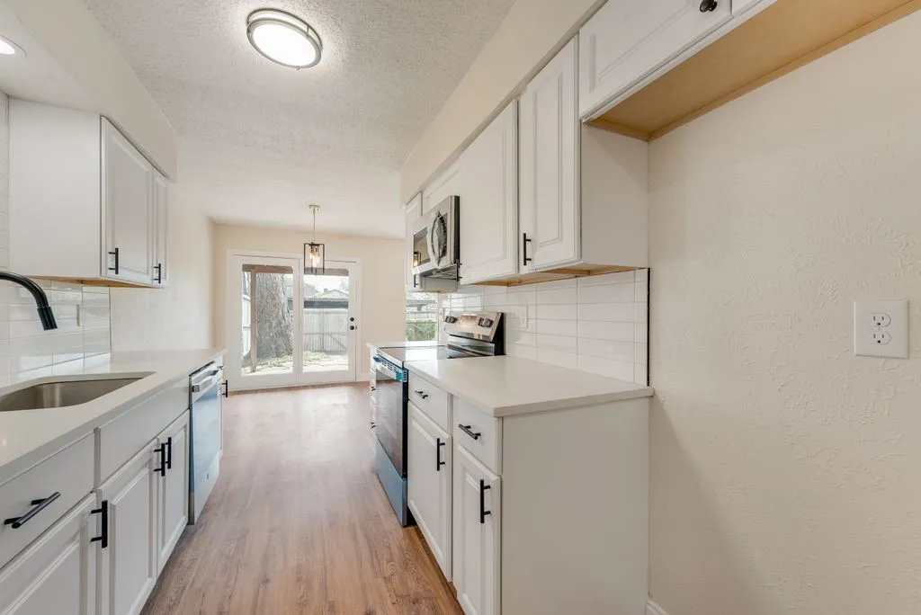 Kitchen featuring white shaker cabinetry, stainless steel appliances, light countertops, wood-finish flooring, and a white subway tile backsplash