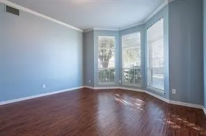 Spare room featuring crown molding, healthy amount of natural light, wood finished floors, and baseboards