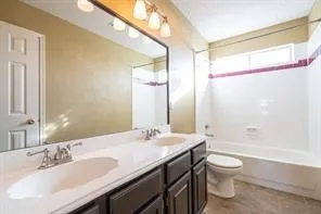 Full bath with toilet, double vanity, and tub / shower combination