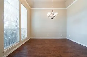 Unfurnished room featuring dark wood-style floors, a chandelier, baseboards, and crown molding