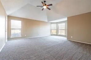 Carpeted empty room featuring vaulted ceiling, baseboards, and ceiling fan