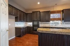 Kitchen with decorative backsplash, dark brown cabinetry, recessed lighting, dark wood-type flooring, and baseboards