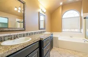 Bathroom with a bath, healthy amount of natural light, tile patterned flooring, vaulted ceiling, and vanity