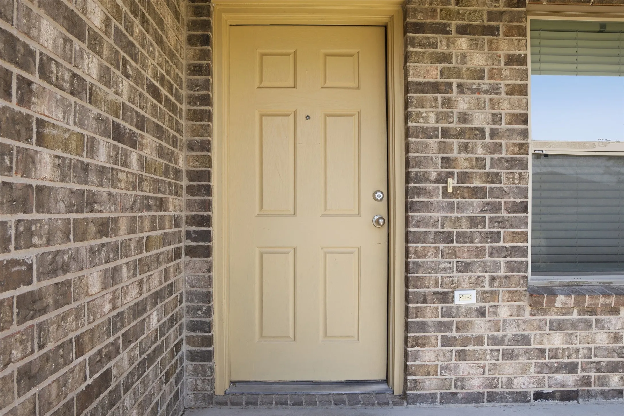 Brick exterior with a paneled entry door and an adjacent window with blinds