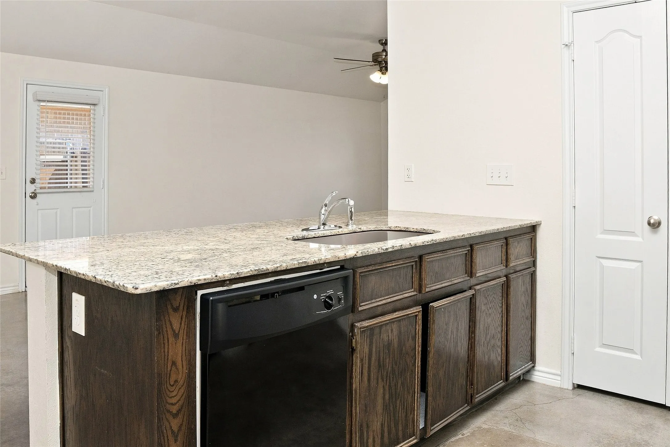 Kitchen island featuring a stainless steel sink, a dishwasher, wood-finish cabinetry, and a light-toned countertop