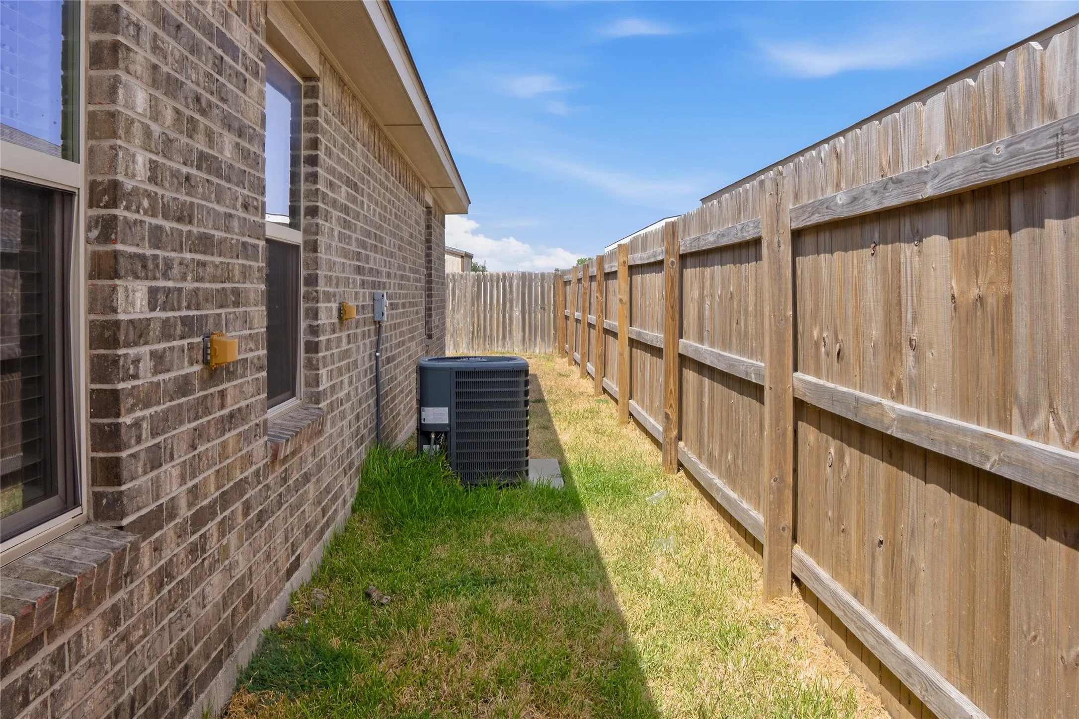 Brick exterior with multiple windows, air conditioning unit, and wood privacy fencing