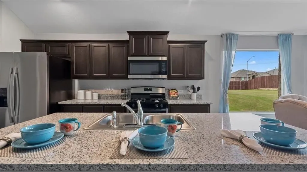 Kitchen featuring a large island with an undermount sink, dark wood cabinetry, stainless steel appliances, and light-colored countertops