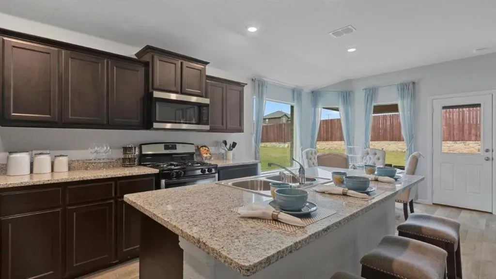 Kitchen featuring dark wood cabinetry, granite countertops, stainless steel appliances, and a central island with an integrated sink