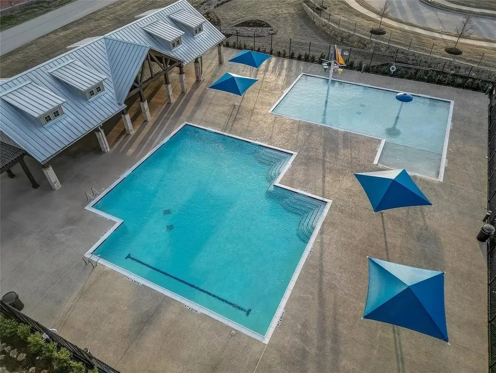 Resort-style pool area featuring two distinct pools, a covered pavilion with exposed beams and dormer windows, and multiple shade structures