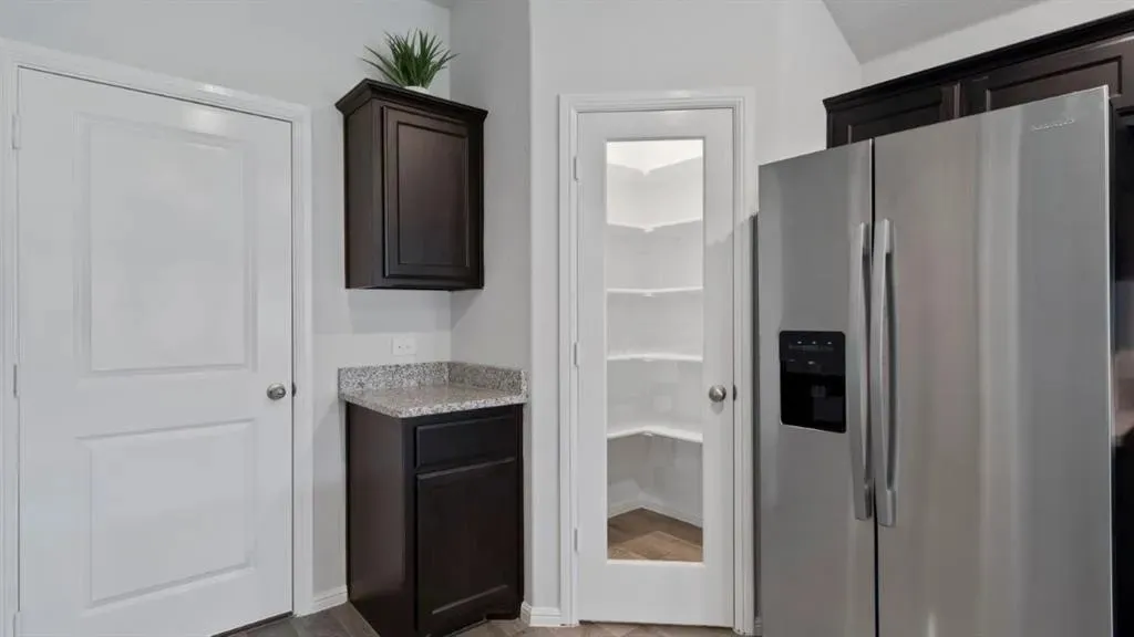 Stainless steel refrigerator, built-in dark wood cabinetry, granite-finish countertop, and a walk-in pantry with a glass-paneled door