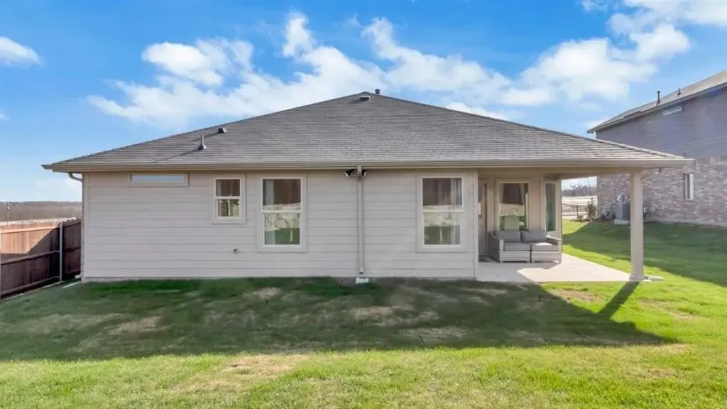 Rear exterior with an expansive lawn, covered patio, and privacy fencing