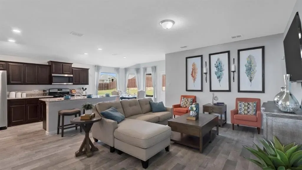 Open-concept living space featuring wood-finish flooring, dark wood cabinetry, stainless steel appliances, a kitchen island with seating, and bay windows