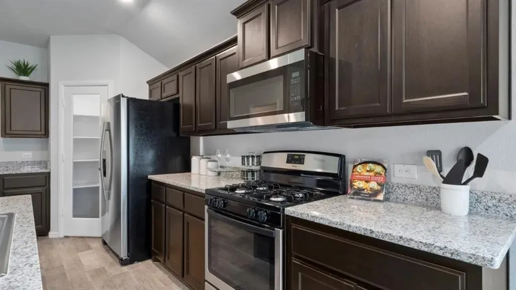 Wood-finish flooring, dark wood cabinetry, light-toned countertops, and stainless steel appliances