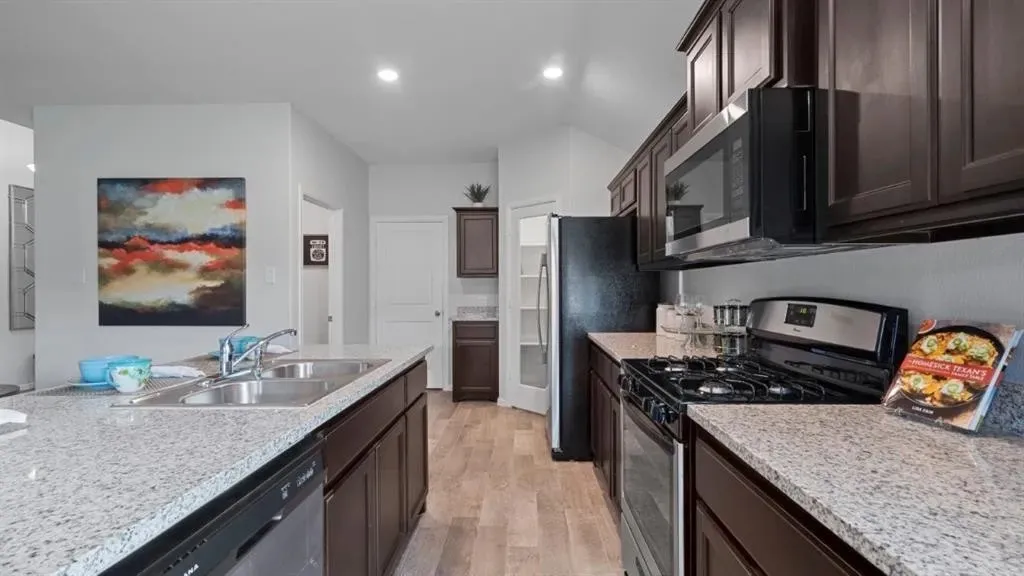 Kitchen featuring dark wood cabinetry, light-toned countertops, stainless steel appliances, and wood-finish flooring