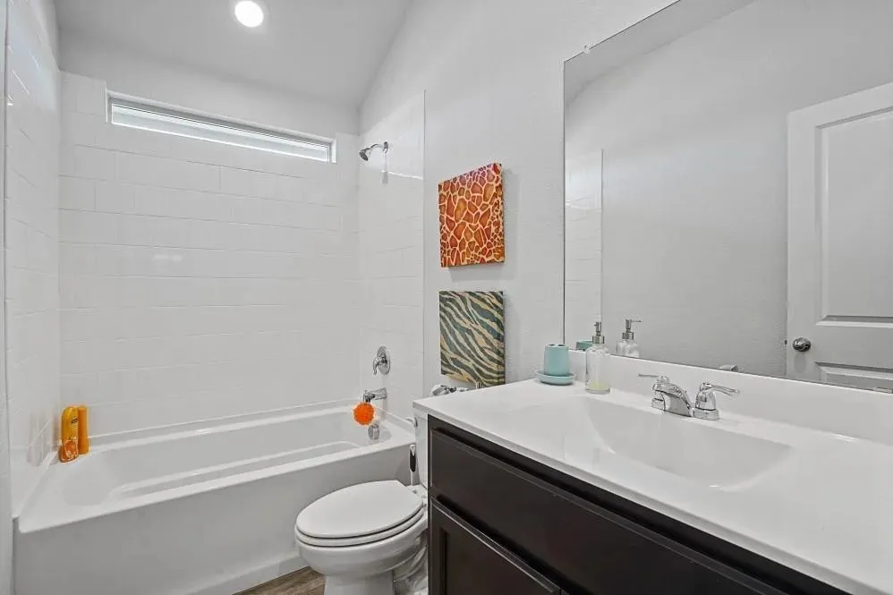Full bathroom featuring a white tub with subway tile surround, a dark wood-finish vanity with an integrated sink, and a large wall-mounted mirror