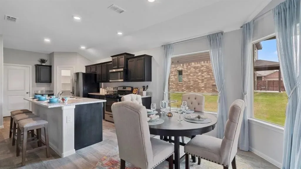 Open-concept kitchen and dining area featuring dark cabinetry, stainless steel appliances, and a kitchen island with seating