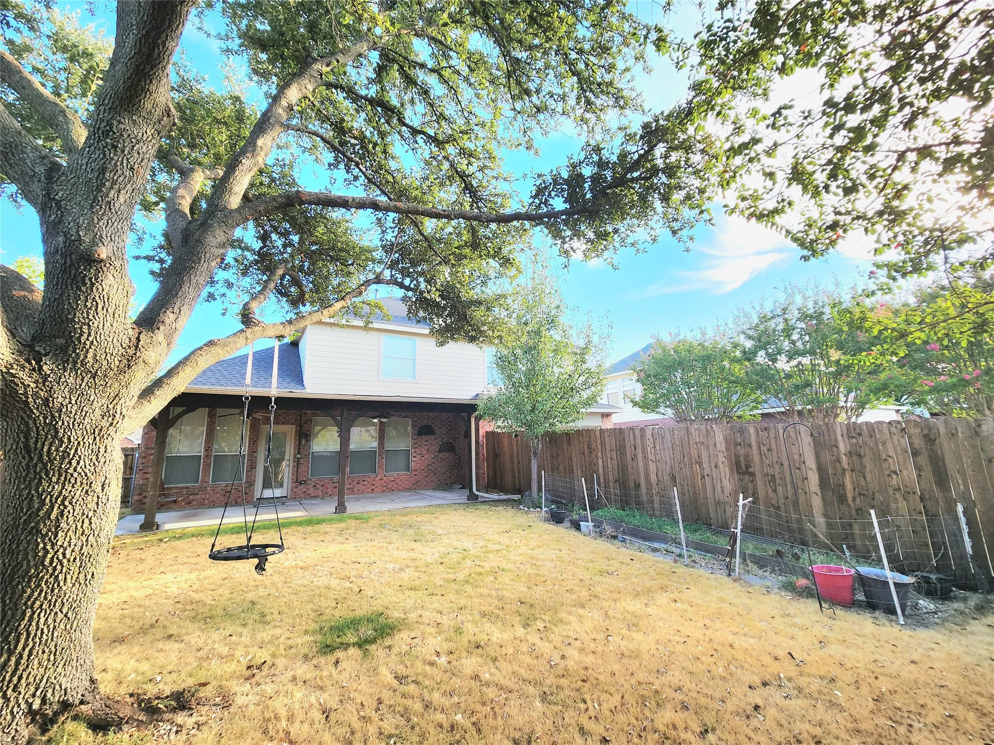 Expansive backyard featuring a mature tree, wood privacy fencing, and a covered patio with exposed beam supports