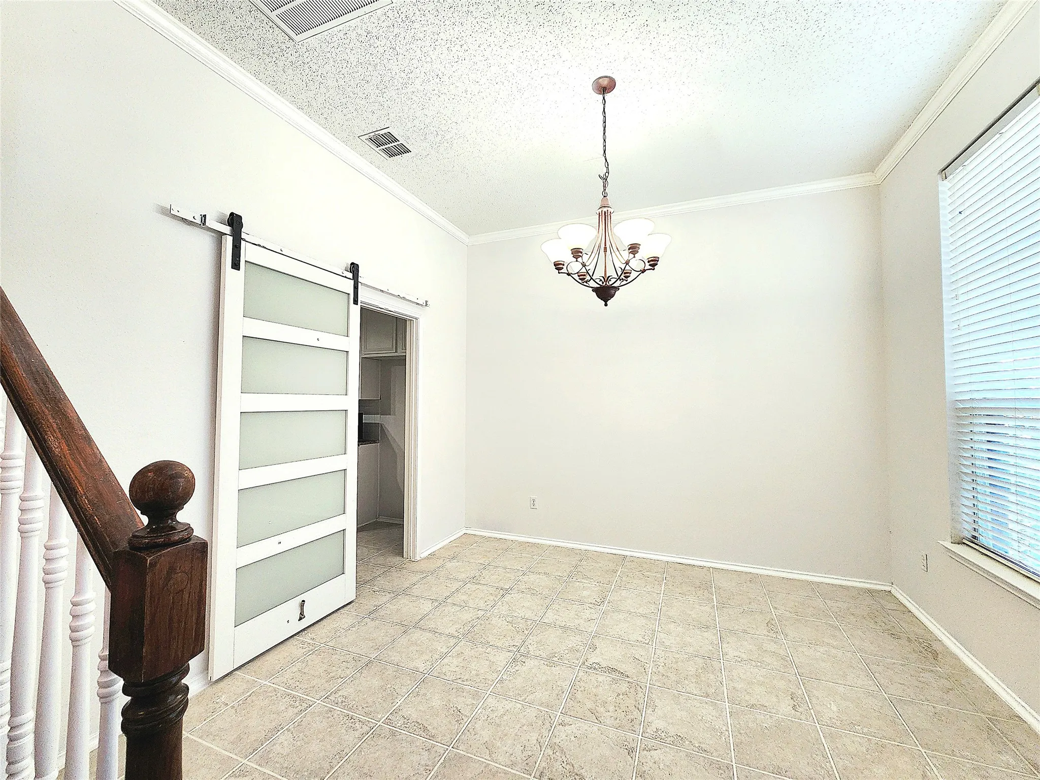 Decorative chandelier, crown molding, white barn door with frosted glass panels, wood staircase with white balusters, and square tile flooring