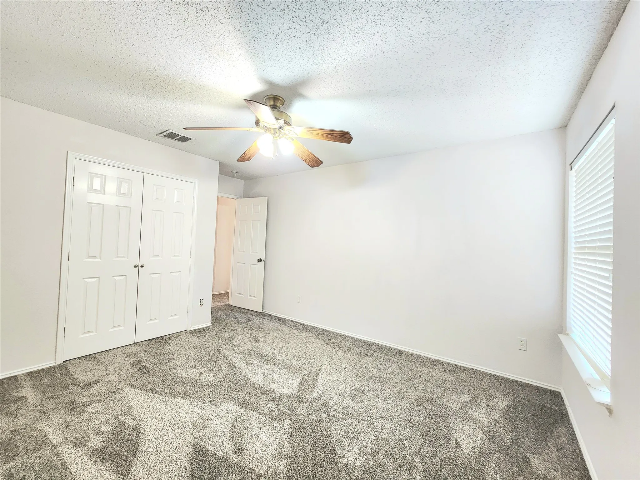 Textured ceiling with a ceiling fan light fixture, white walls, and gray patterned carpeting