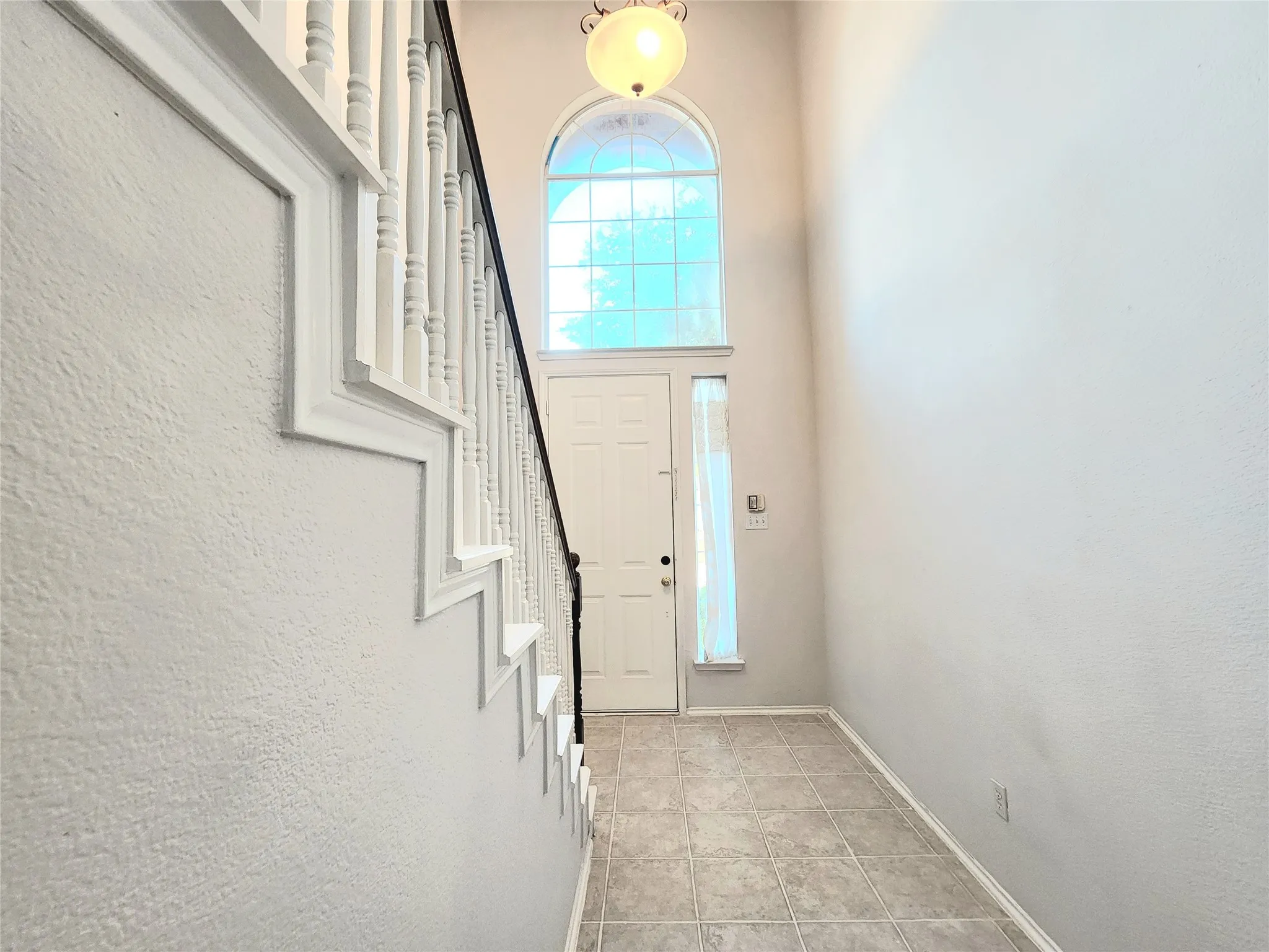Two-story entryway featuring a decorative arch window and tiled flooring