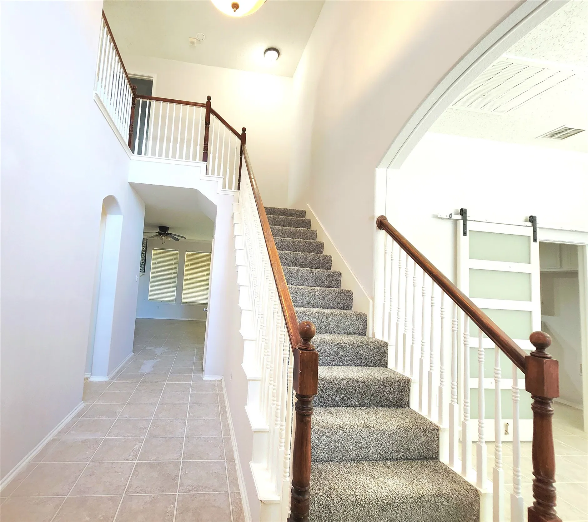 Two-story entryway featuring carpeted stairs with wood newel posts and banister, an arched doorway, and tile flooring