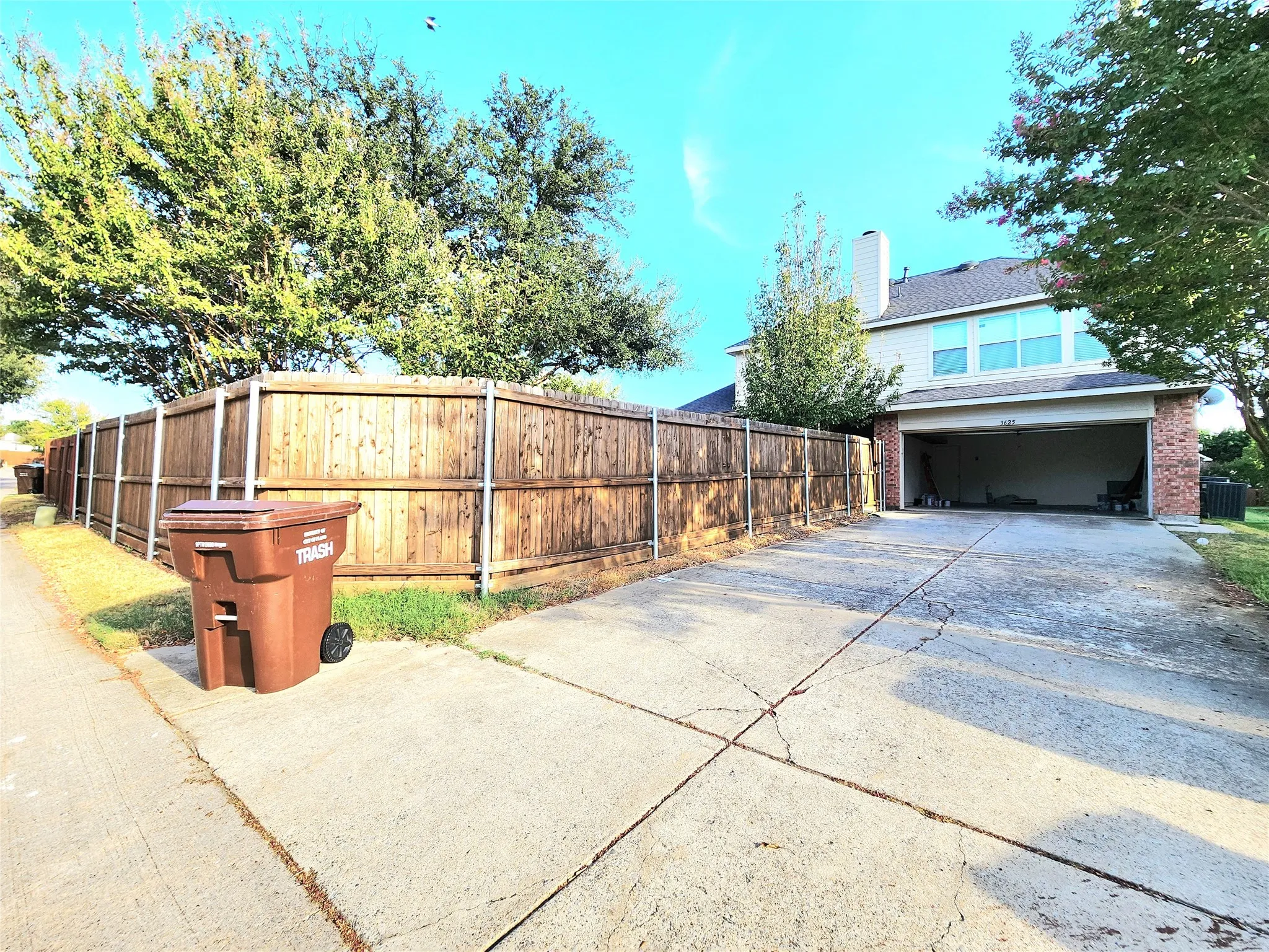Attached two-car garage with a concrete driveway, brick facade, and wood fencing