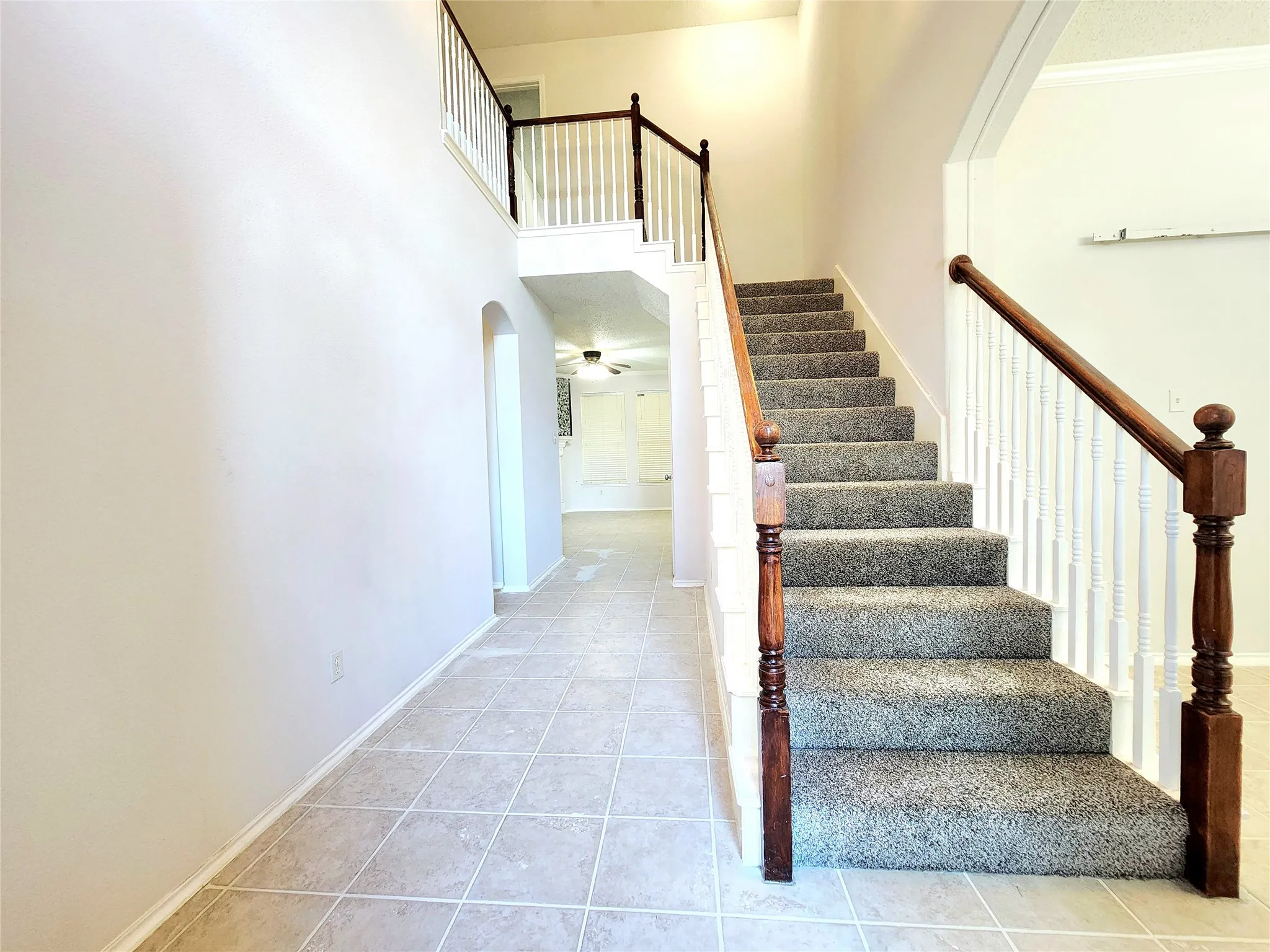 Two-story entryway featuring tile flooring, a carpeted staircase with wood handrails, and a second-story landing with a white spindle railing