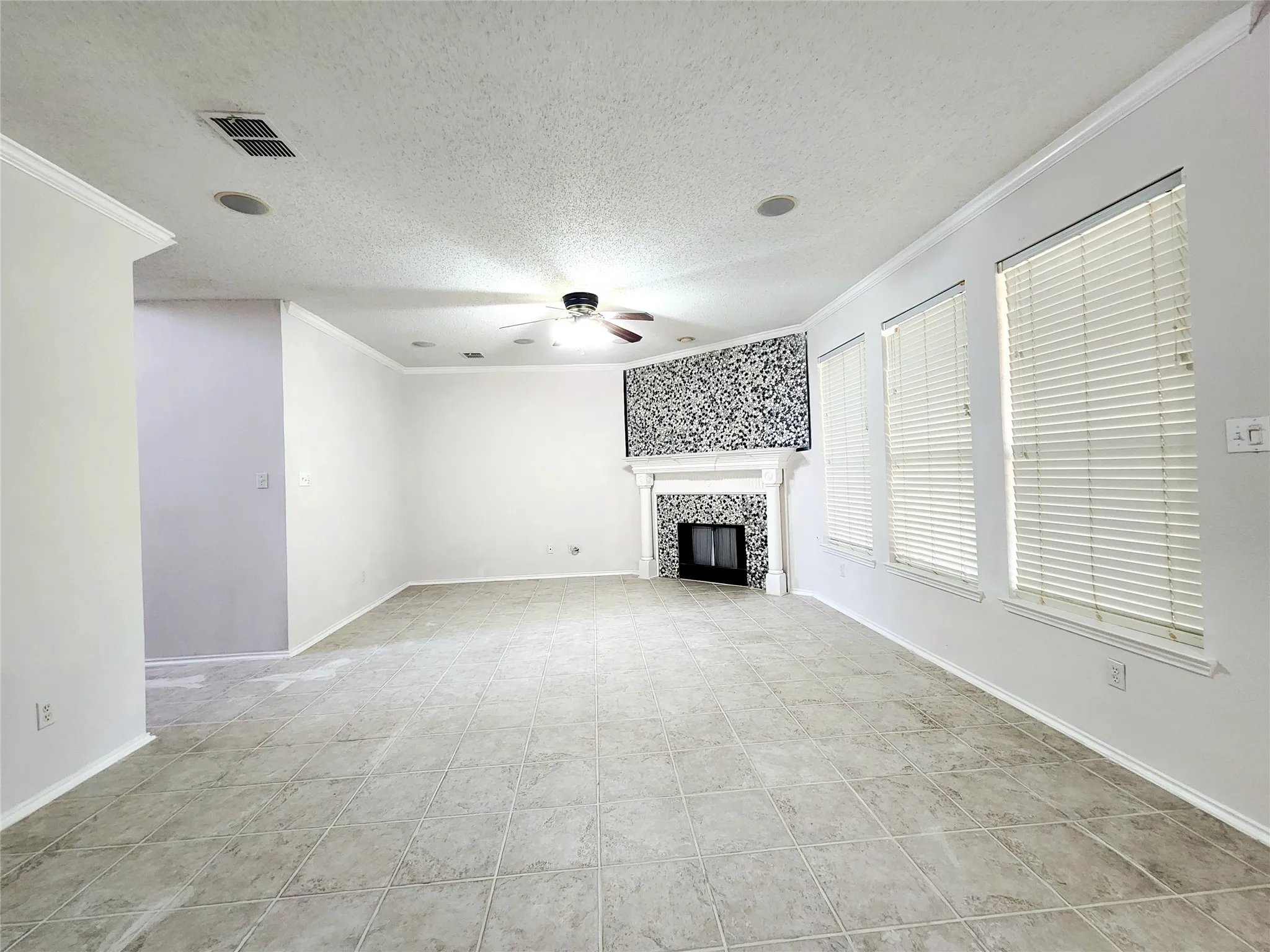Tiled flooring, crown molding, built-in fireplace with decorative mantel, ceiling fan, and multiple windows with blinds