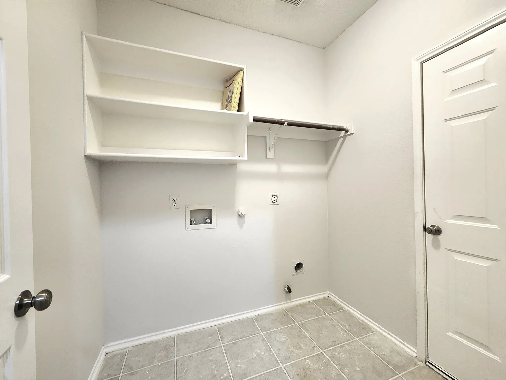 Laundry area featuring light-toned tile flooring, built-in shelving, and a wall-mounted hanging rod