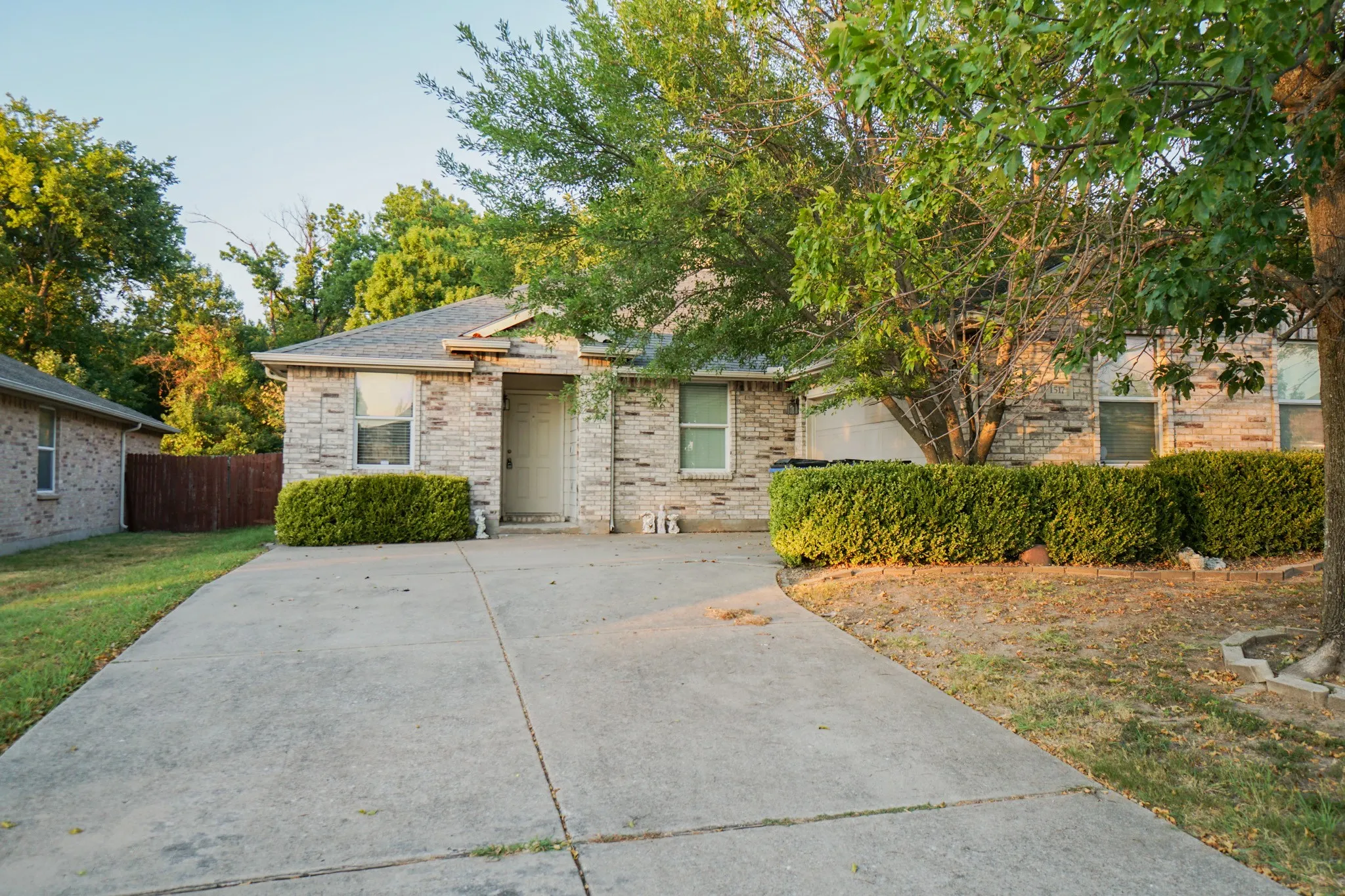 Stone veneer exterior with mature trees, concrete driveway, and established shrubbery