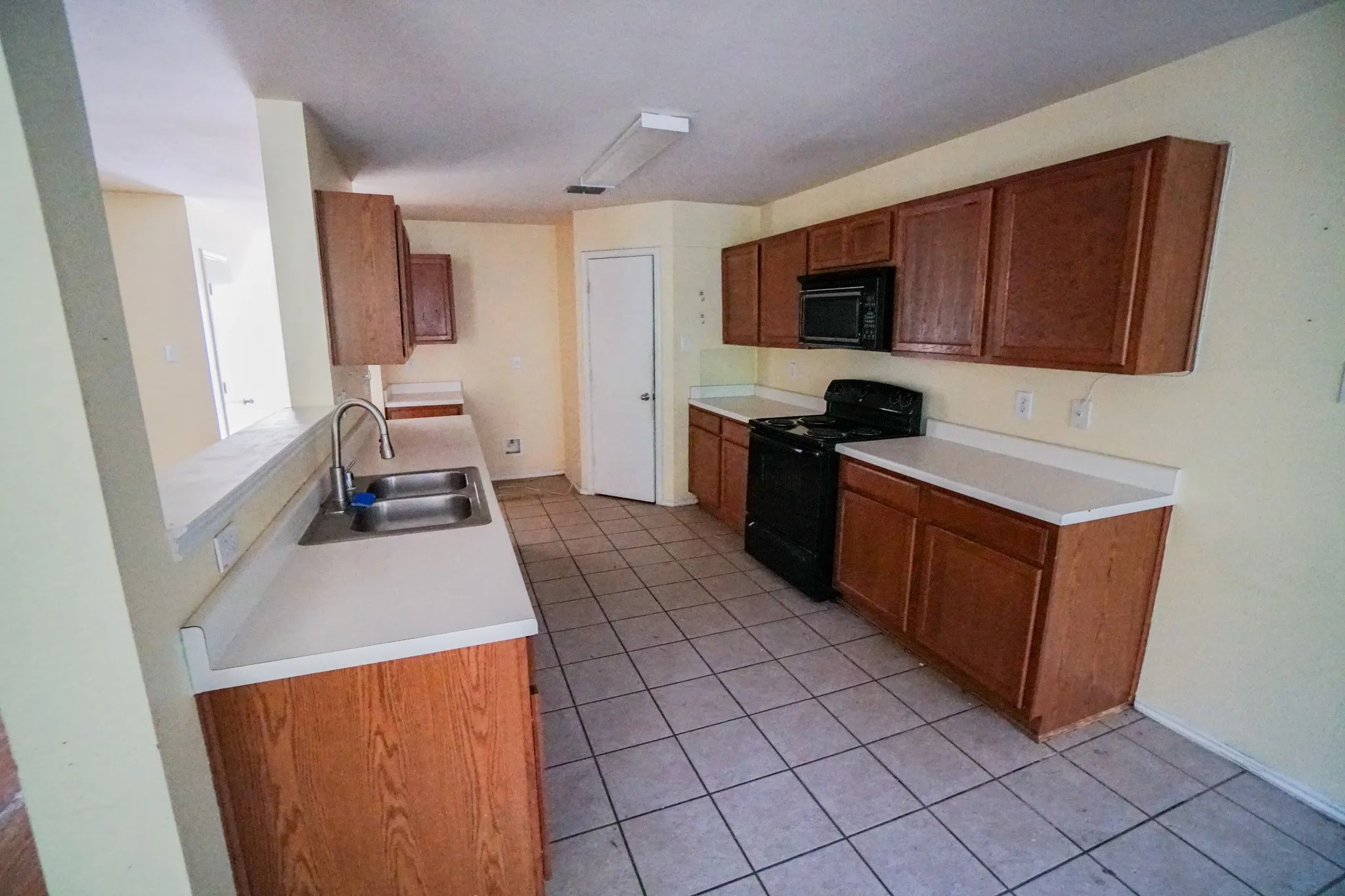 Kitchen featuring wood-finish cabinetry, white countertops, a double basin sink, black range, and tile flooring