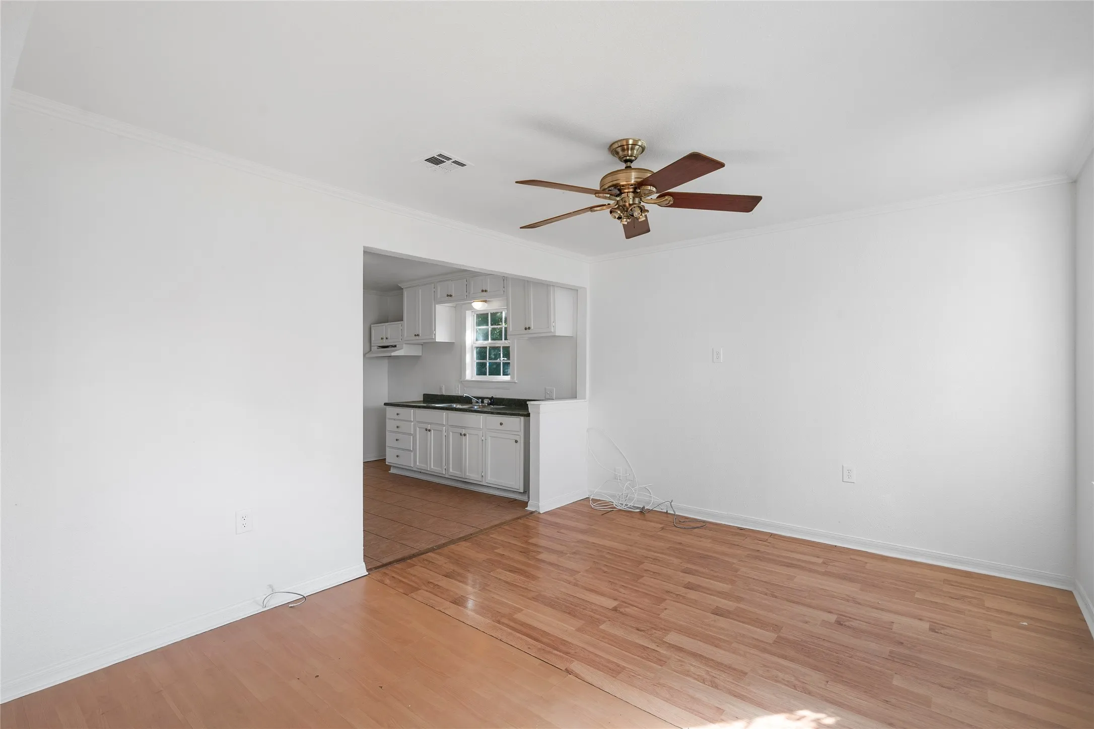 Unfurnished living room featuring ornamental molding, a ceiling fan, and light wood-type flooring