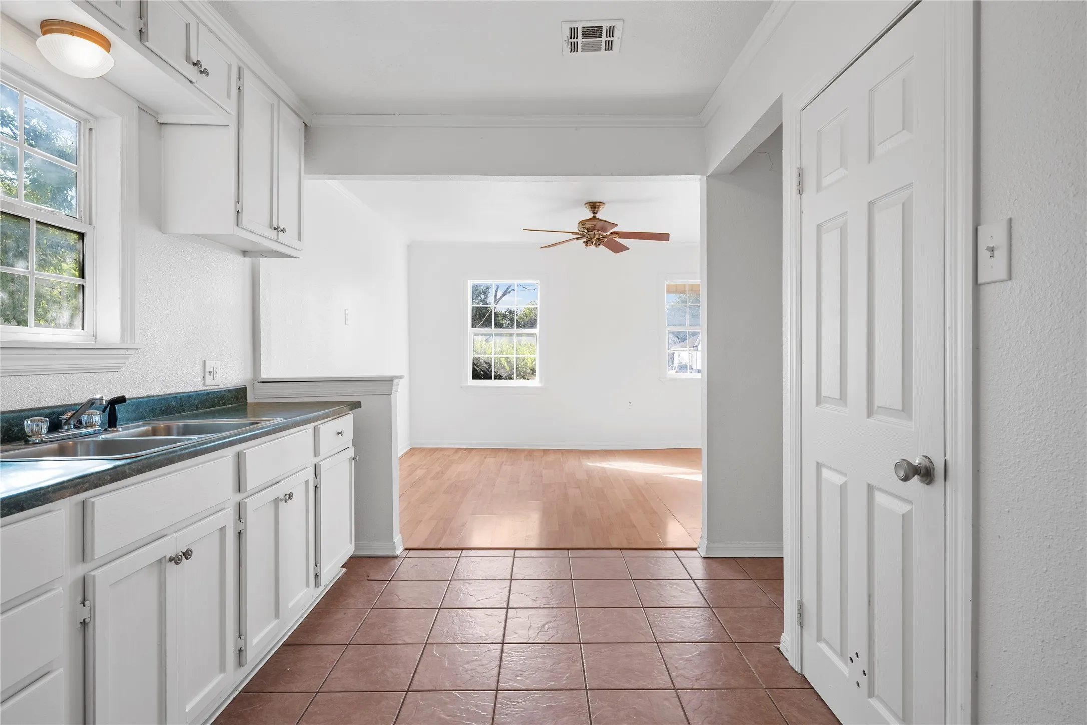 Kitchen with dark countertops, white cabinets, ceiling fan, tile patterned flooring, and crown molding