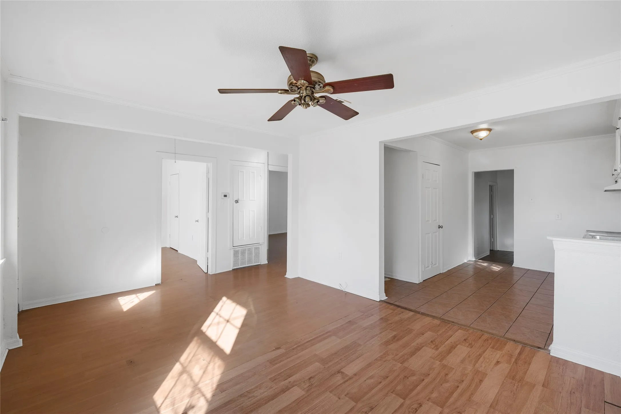 Unfurnished living room featuring ornamental molding, ceiling fan, and light wood-type flooring