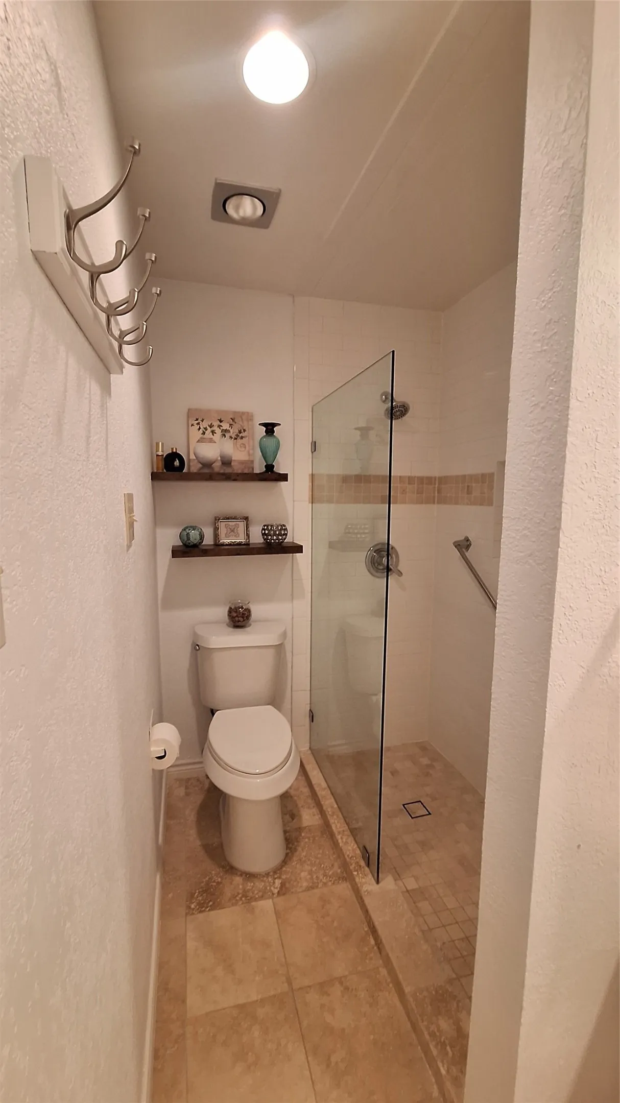 tumbled marble shower with framless glass, floating shelves above new toilet