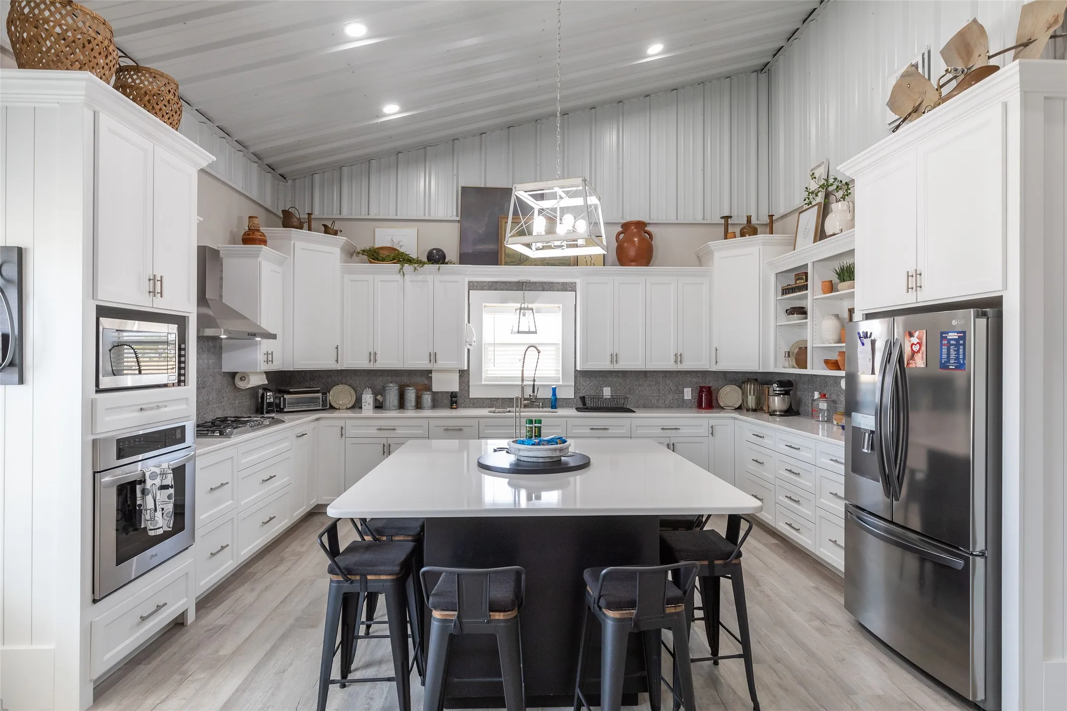 Vaulted ceiling kitchen featuring white cabinetry, a center island with seating, integrated stainless steel appliances, and wood-finish flooring