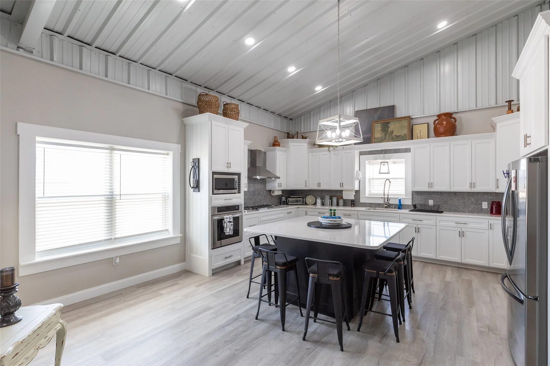 Spacious kitchen featuring white cabinetry, a large kitchen island with seating, integrated stainless steel appliances, and wood-finish flooring