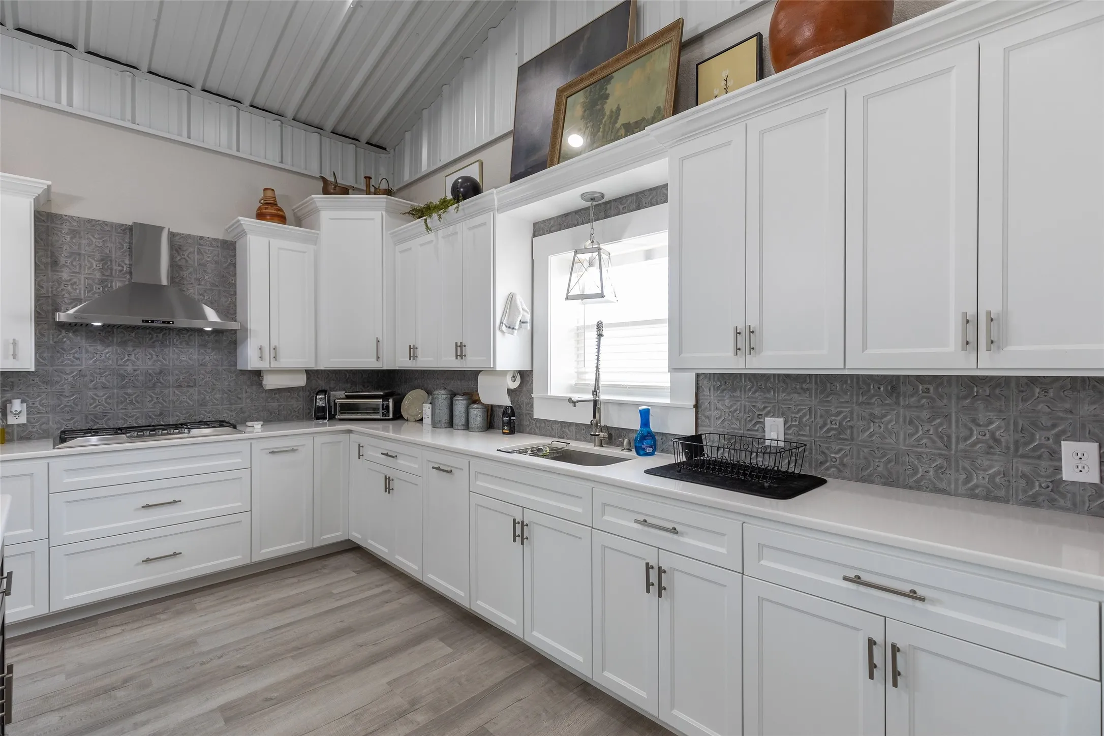 Modern kitchen featuring white shaker cabinetry, stainless steel range hood, stone-finish countertops, decorative tile backsplash, and wood-look flooring