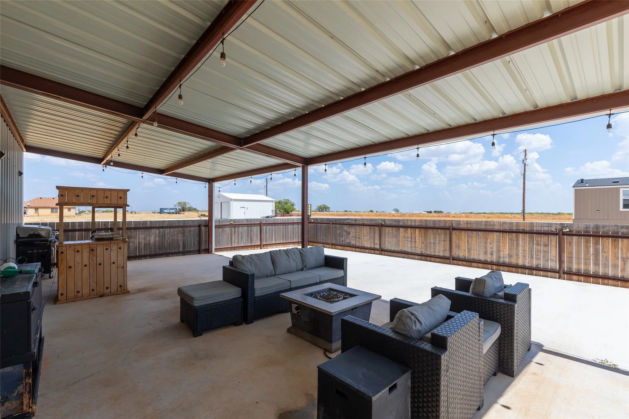 Expansive covered patio featuring a metal roof, string lighting, concrete flooring, and privacy fencing