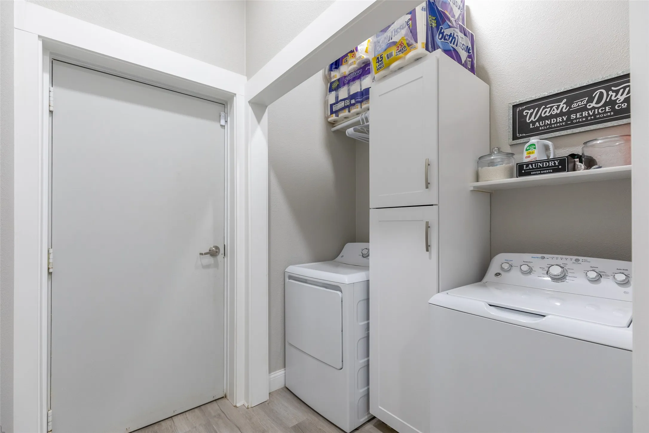 Laundry area featuring wood-finish flooring, white cabinetry, and an integrated shelf