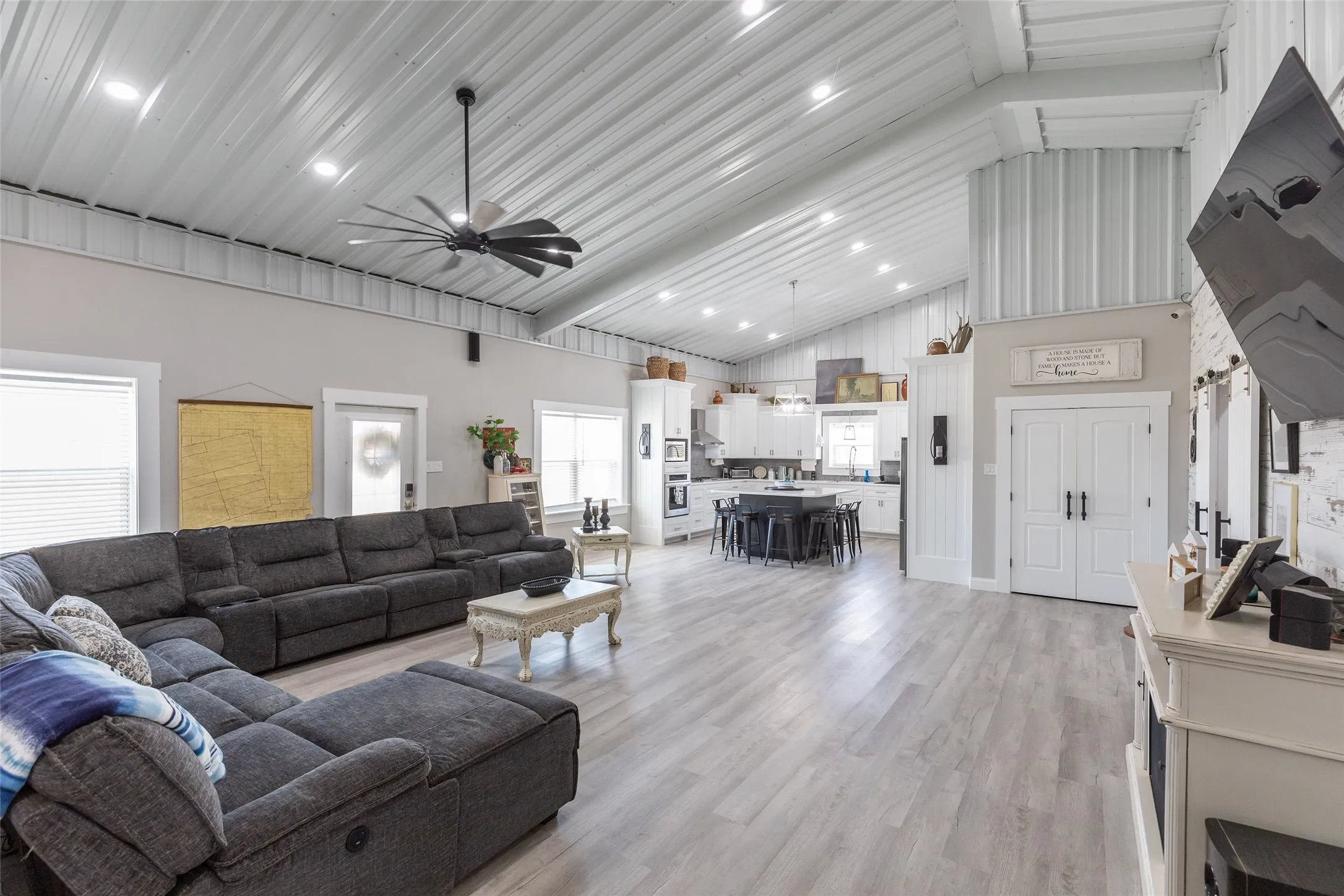 Vaulted corrugated metal ceiling with recessed lighting, wood-finish flooring, white kitchen cabinetry, kitchen island with seating, and double interior doors
