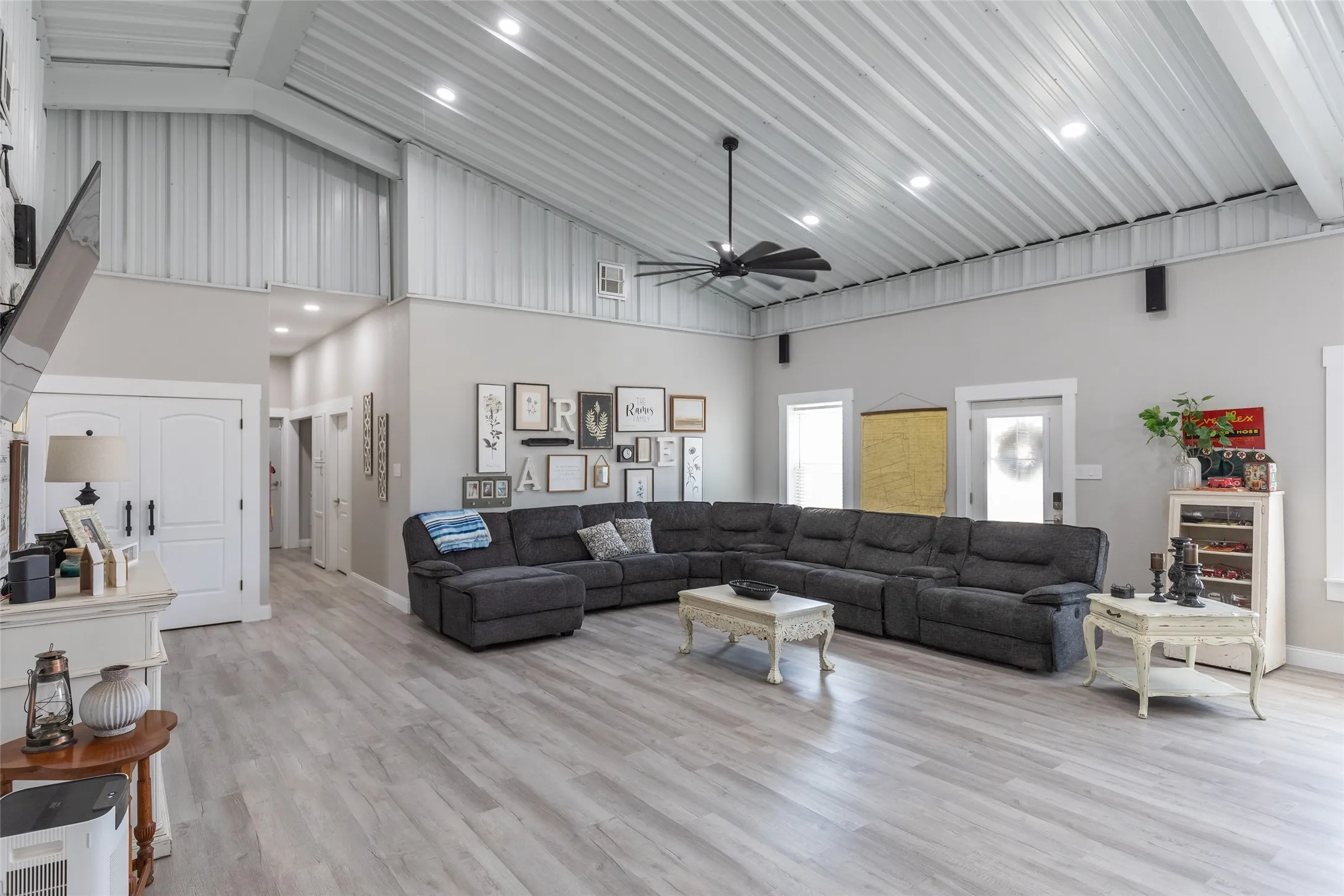 Open-concept living space anchored by a sectional layout, featuring vaulted ceilings with exposed beam detailing, recessed lighting throughout, and wide-plank wood-finish flooring