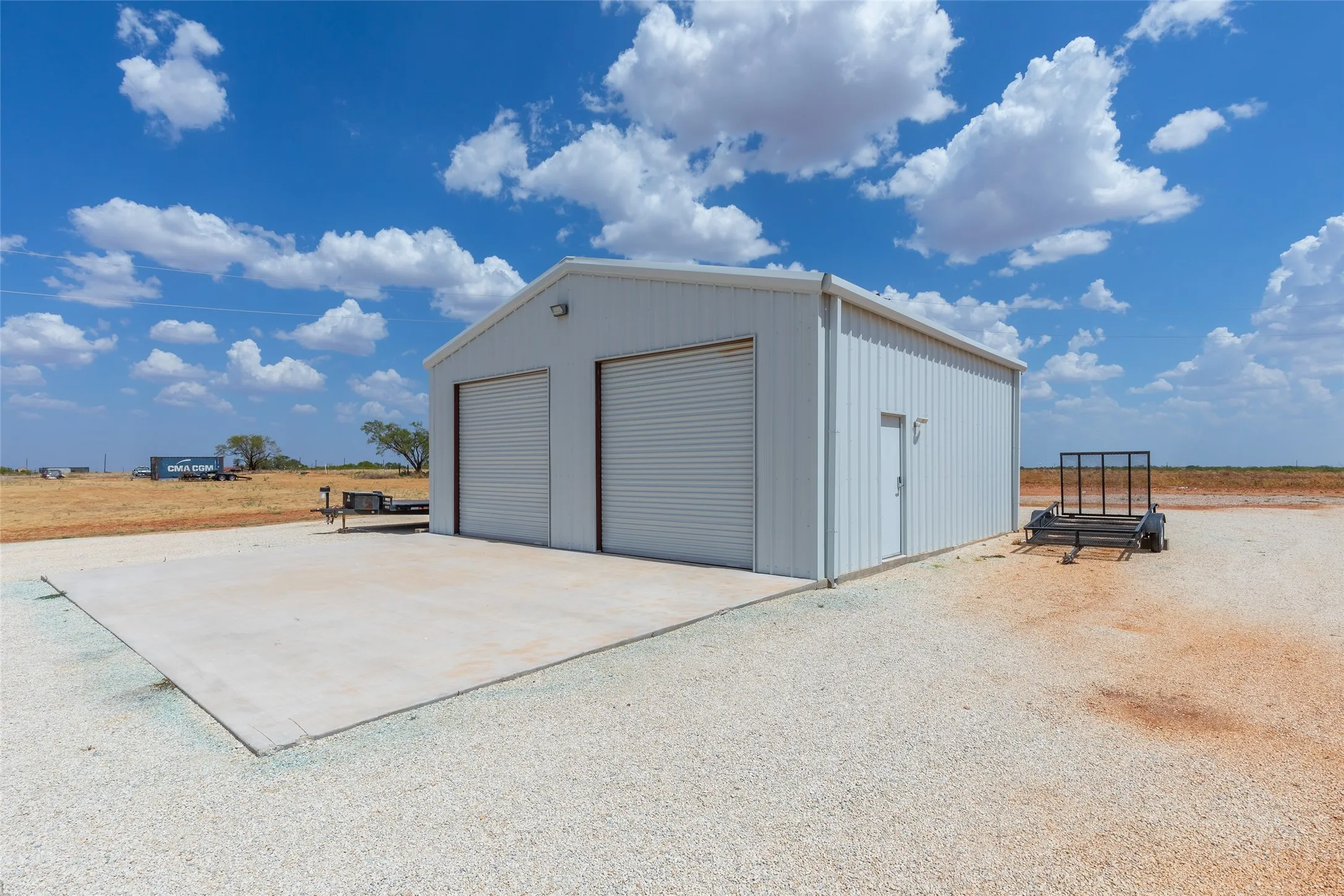 Metal-sided structure with a gabled roof, two roll-up garage doors, a pedestrian entrance, and an expansive concrete pad