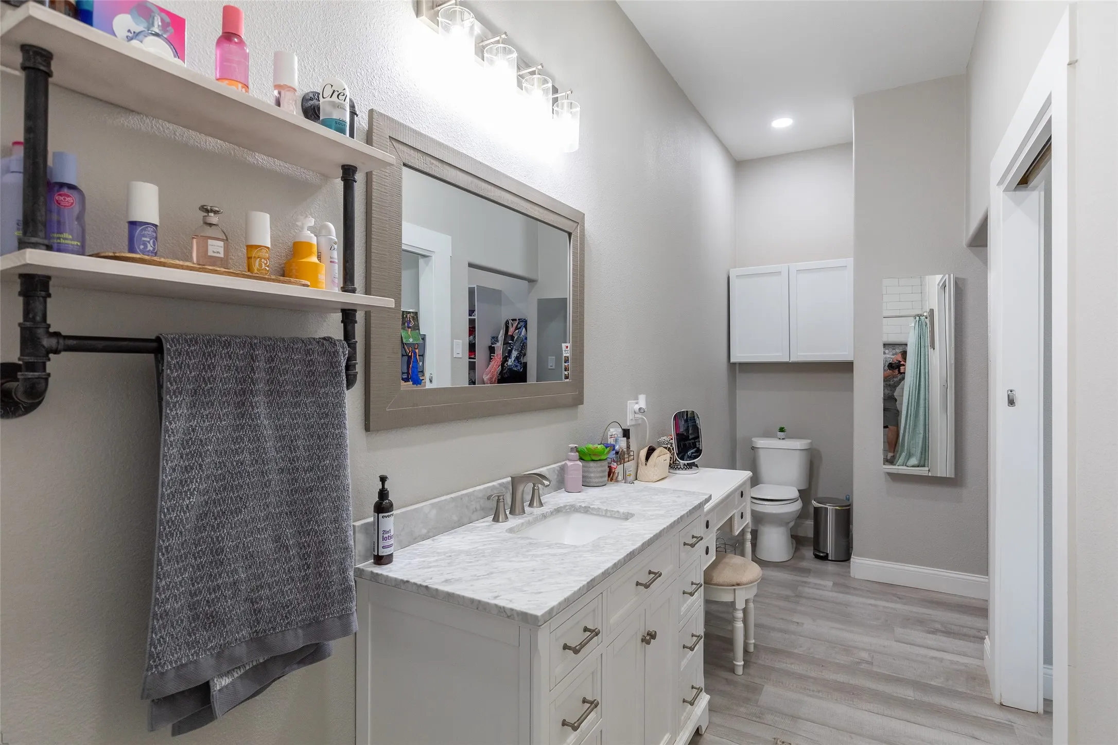 White vanity with dual sinks and chrome fixtures, complemented by a large framed mirror and industrial-style shelving