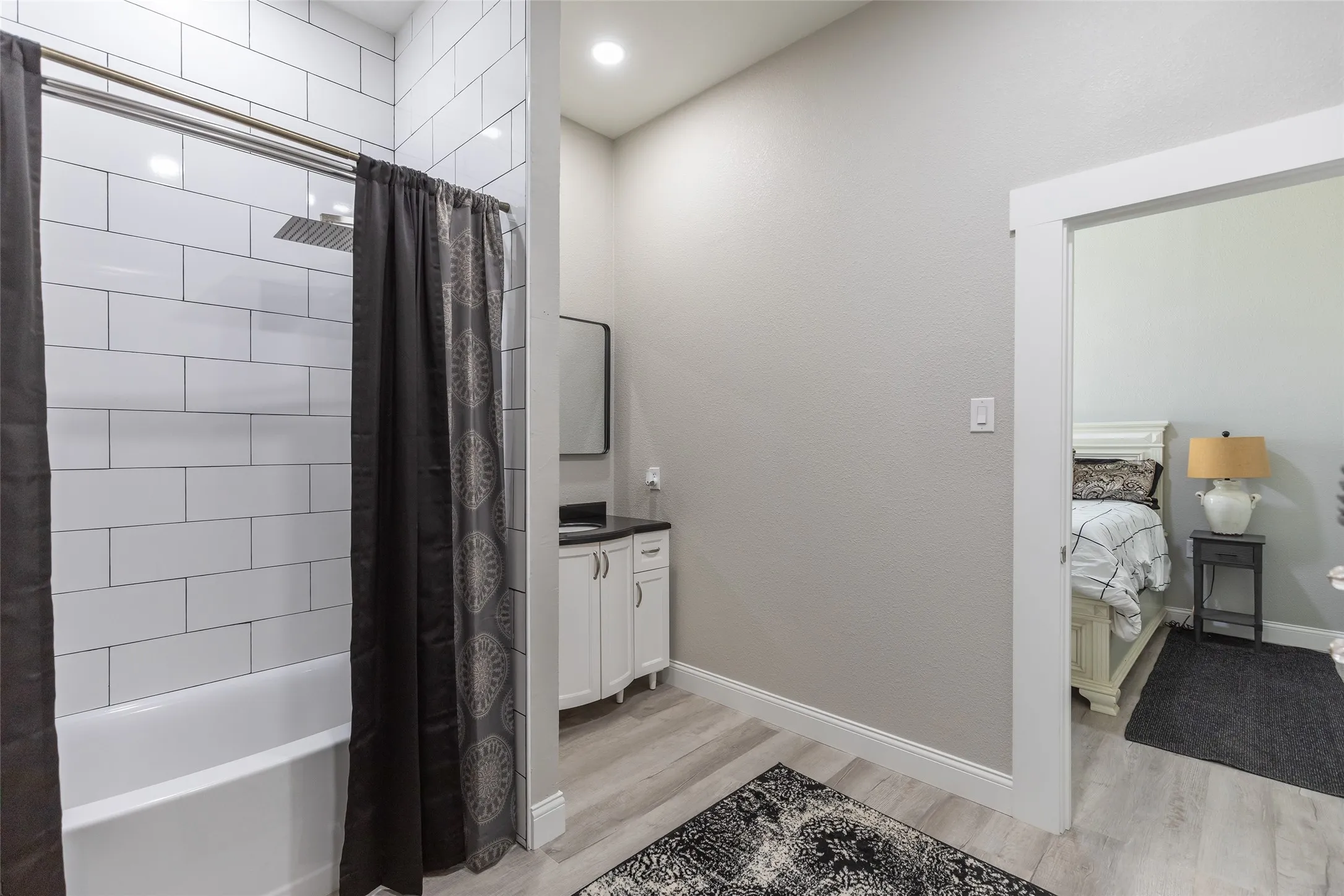Tub and shower combination with subway tile surround, single vanity with dark countertop, and wood-finish flooring