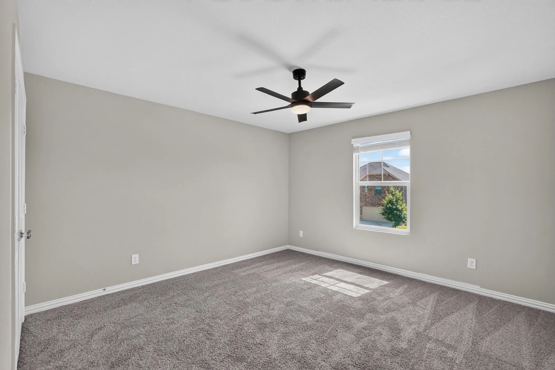 Recessed window with blinds, overhead ceiling fan with lighting, light gray painted walls, and gray carpeted flooring