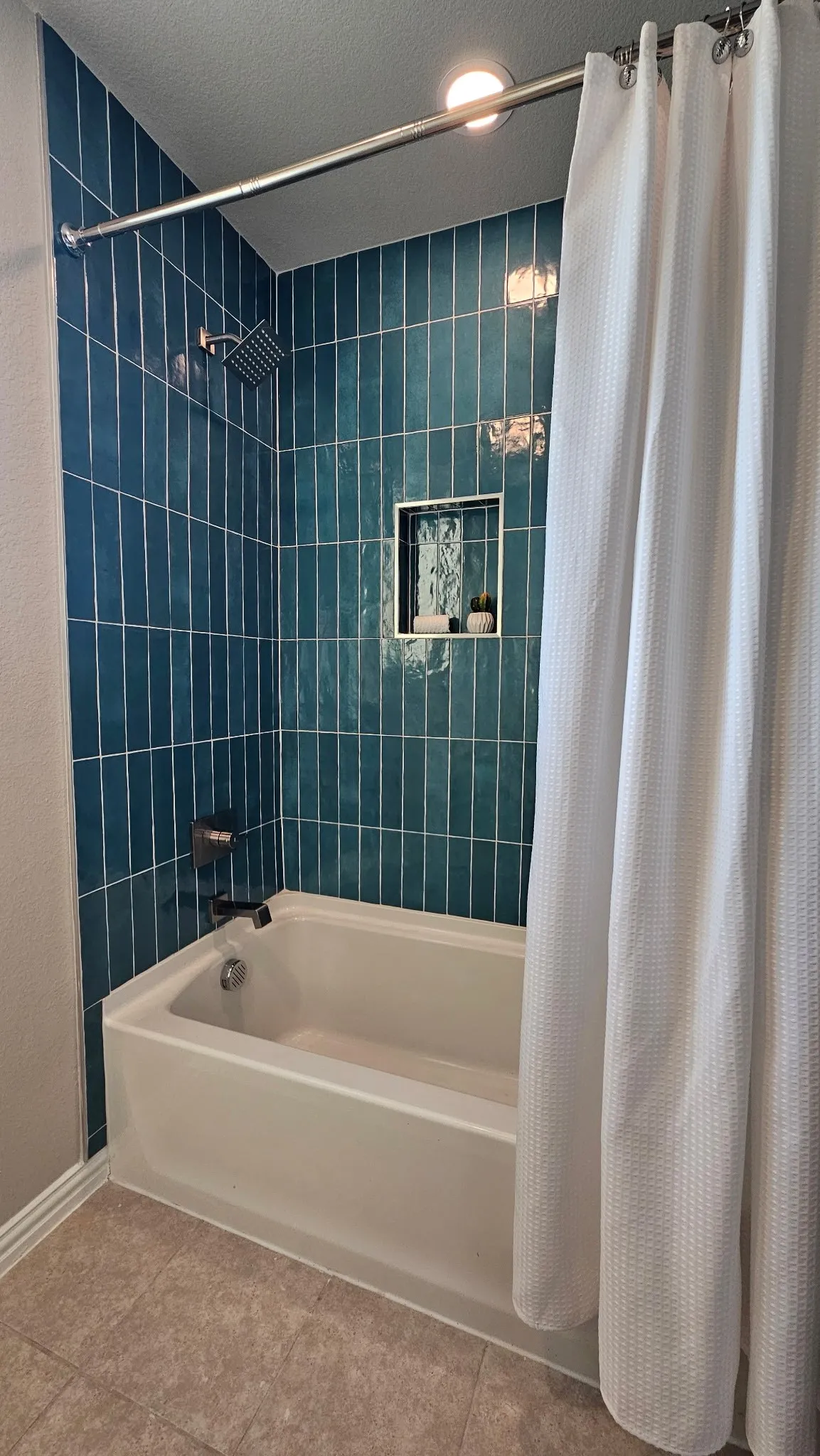 Bathtub with a vertical-stacked teal tile surround, recessed shower niche, and a rain showerhead