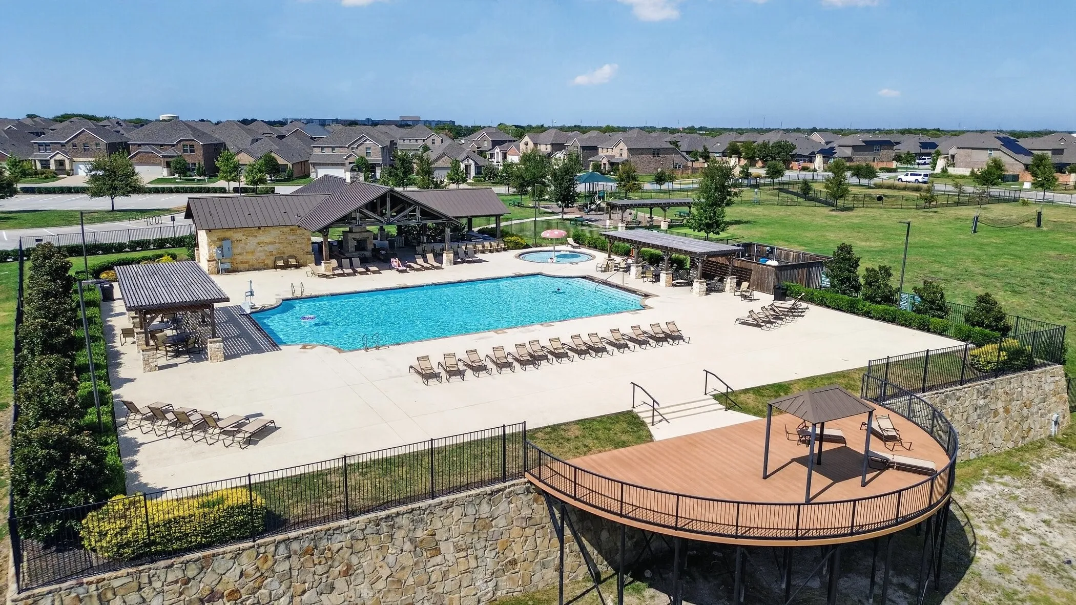 Community pool area featuring a large swimming pool, a covered pavilion with stone accents, a spa, and multiple lounging areas