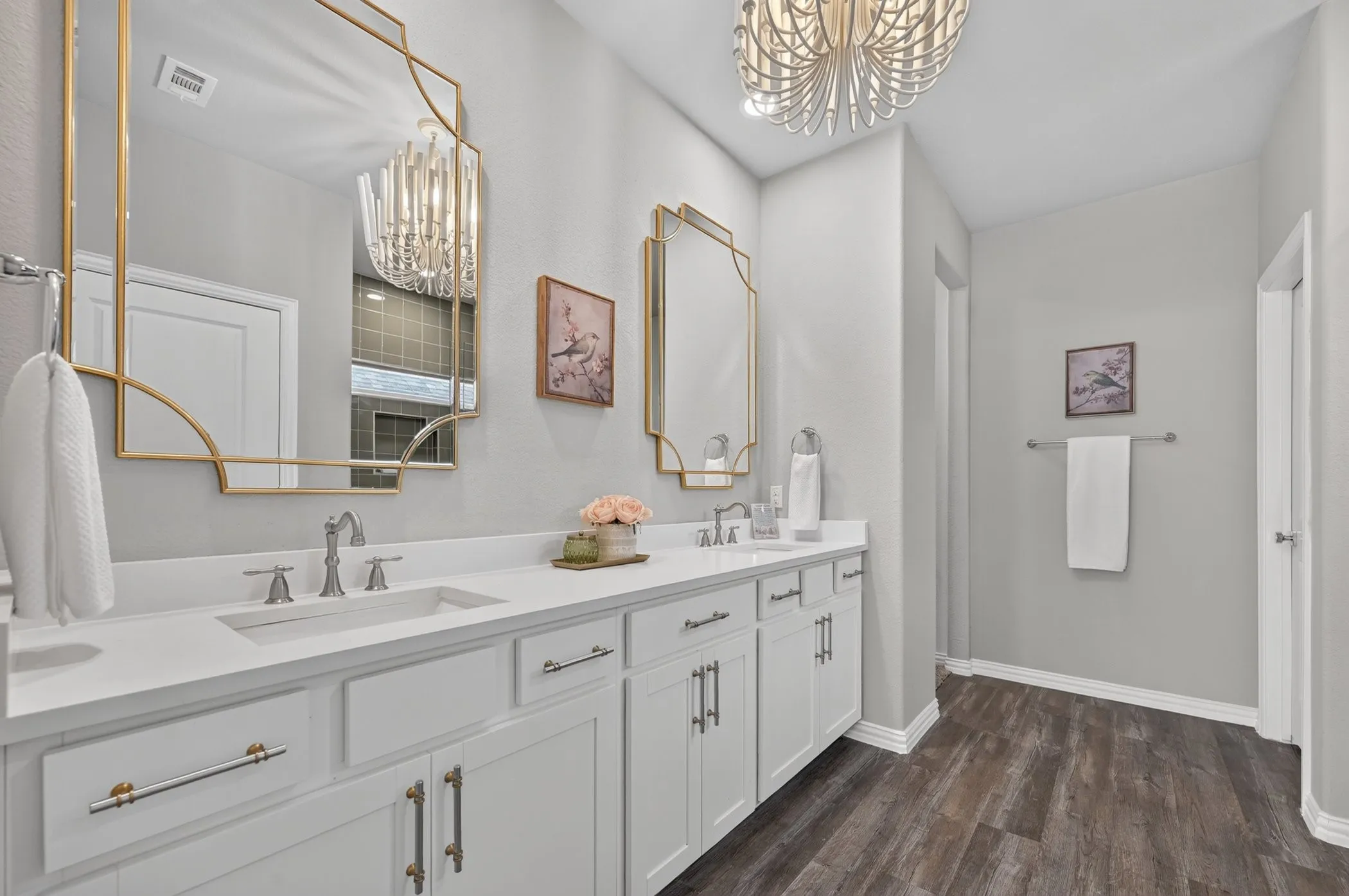 Dual vanity with white cabinetry and integrated sinks, complemented by gold-framed mirrors and a distinctive overhead light fixture