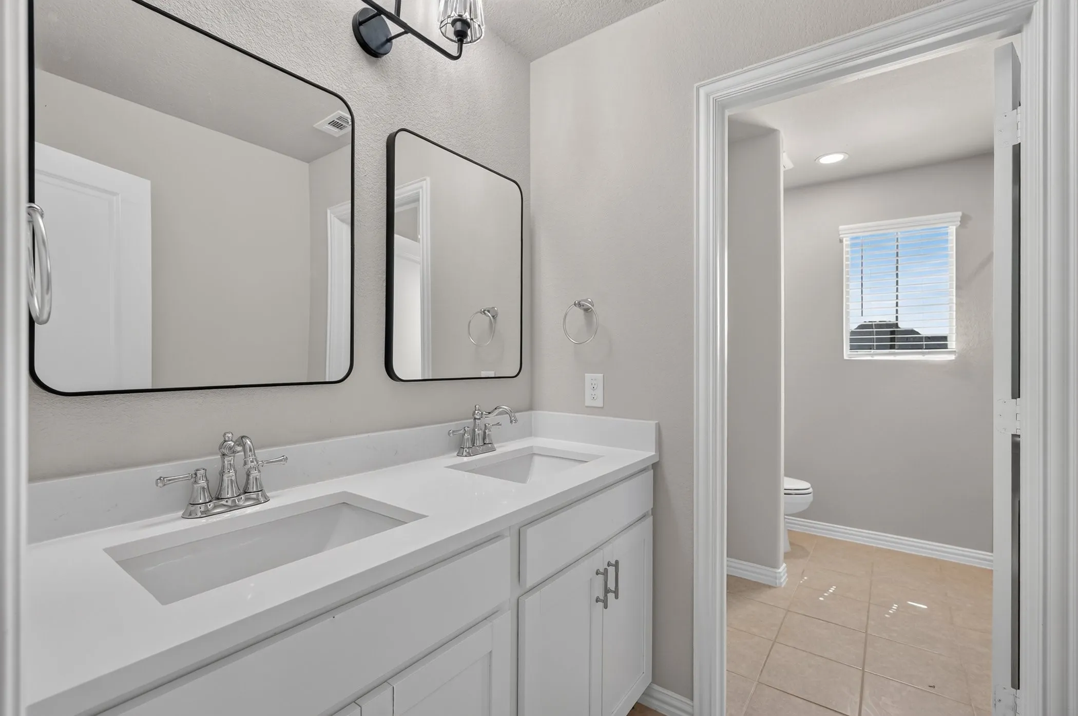 Dual undermount sinks with chrome fixtures, white vanity cabinetry, and dark-framed rectangular mirrors